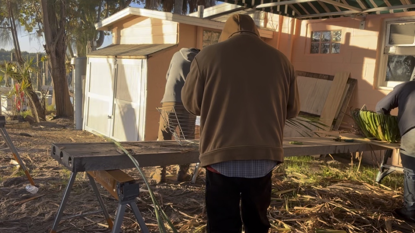 Three crew members weaving nest baskets at a workbench under the canopy
